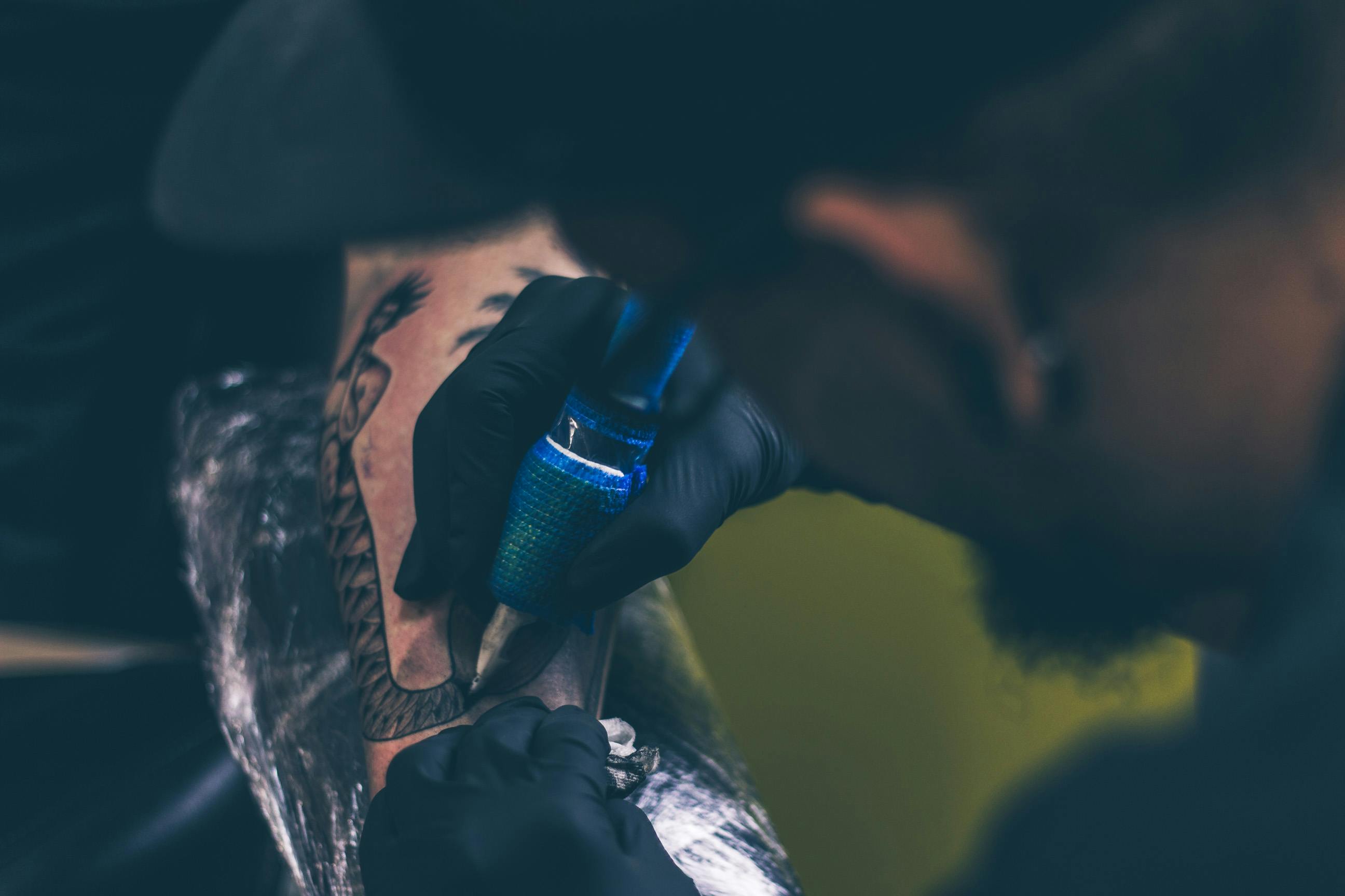 Tatuador fazendo um traço em uma tatuagem onde um homem tem rabo de cobra.