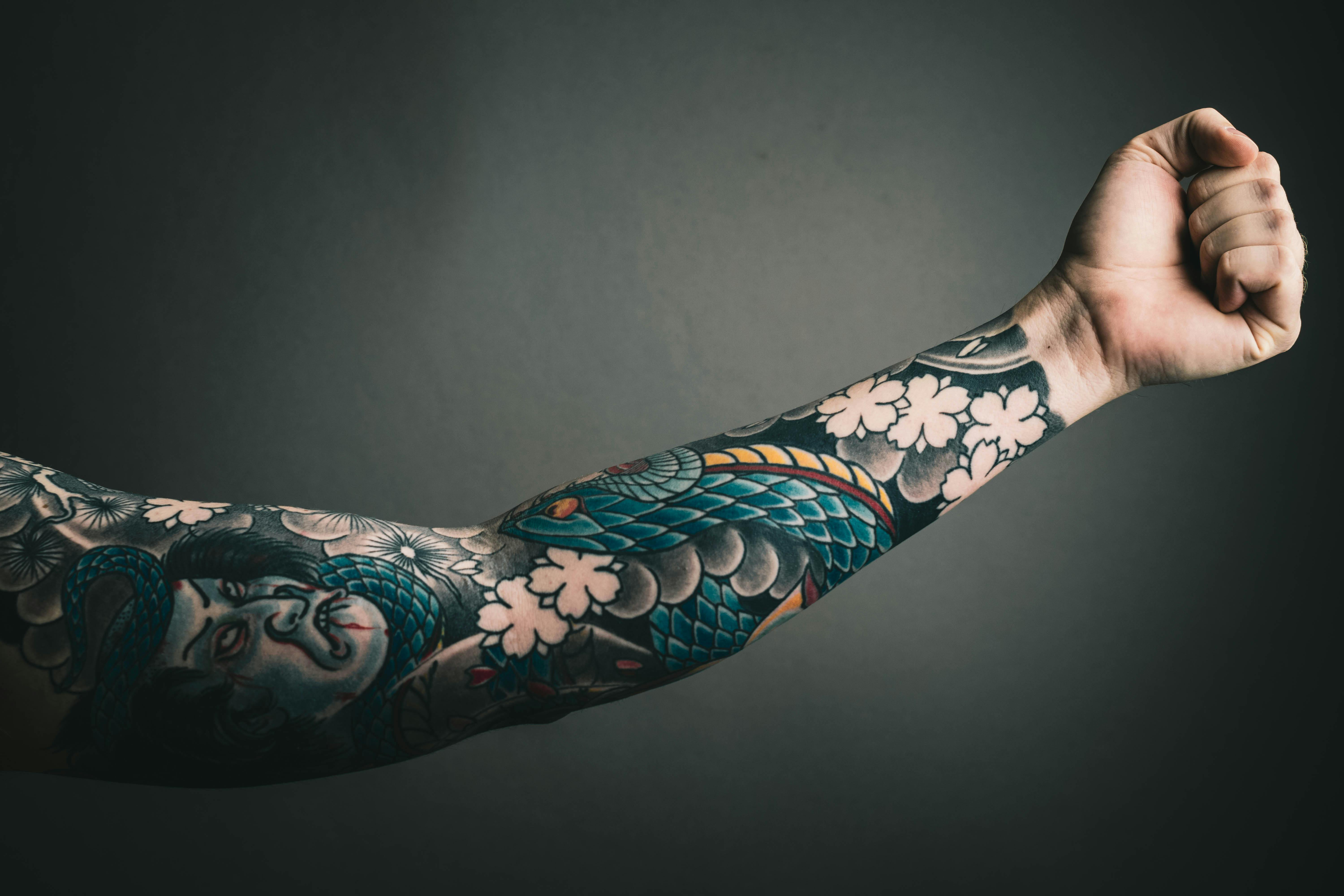 Braço tatuado com um rosto de um japonês e um dragão.