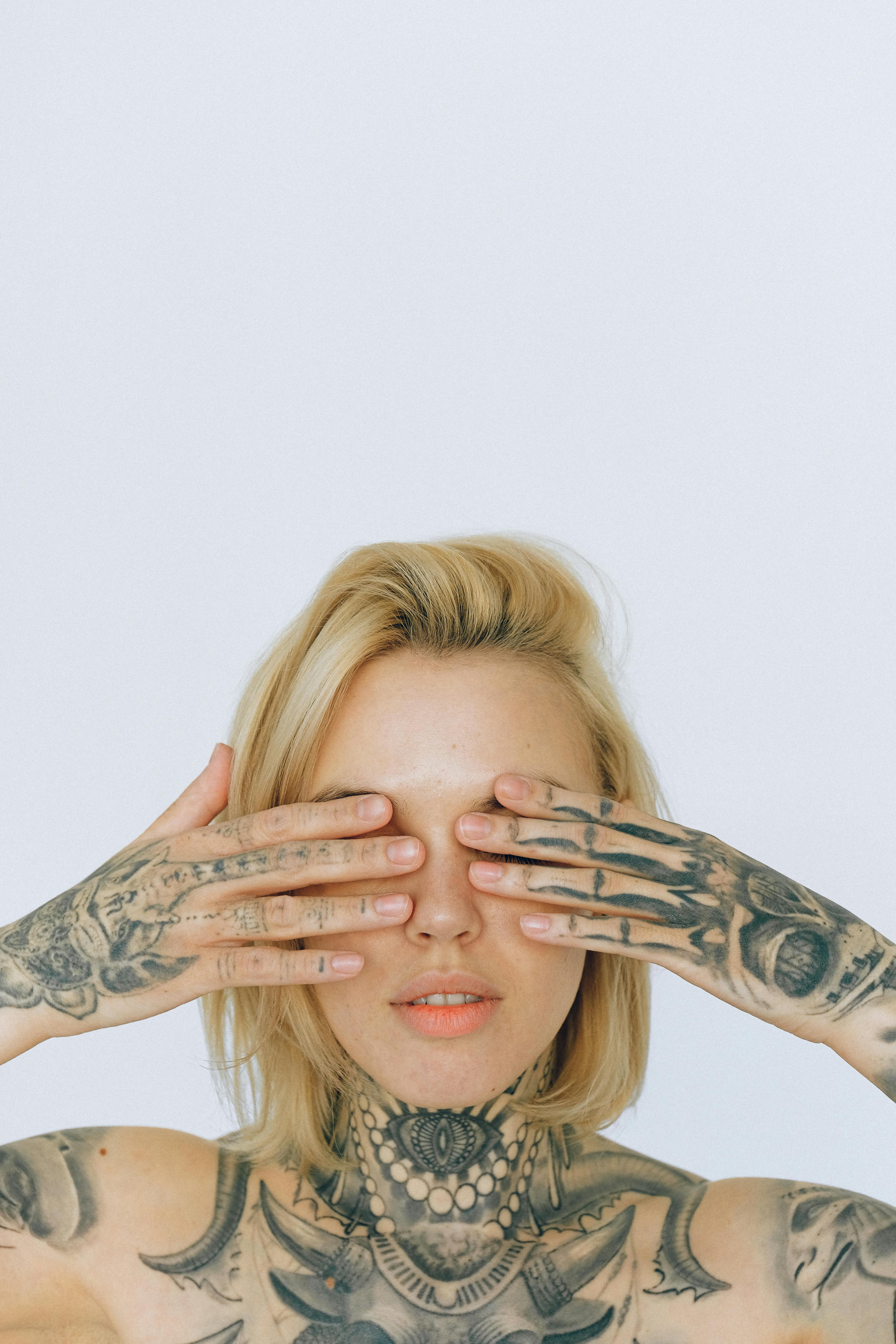 mulher tapando os olhos e mostrando diversas tatuagens pequenas em preto e cinza.