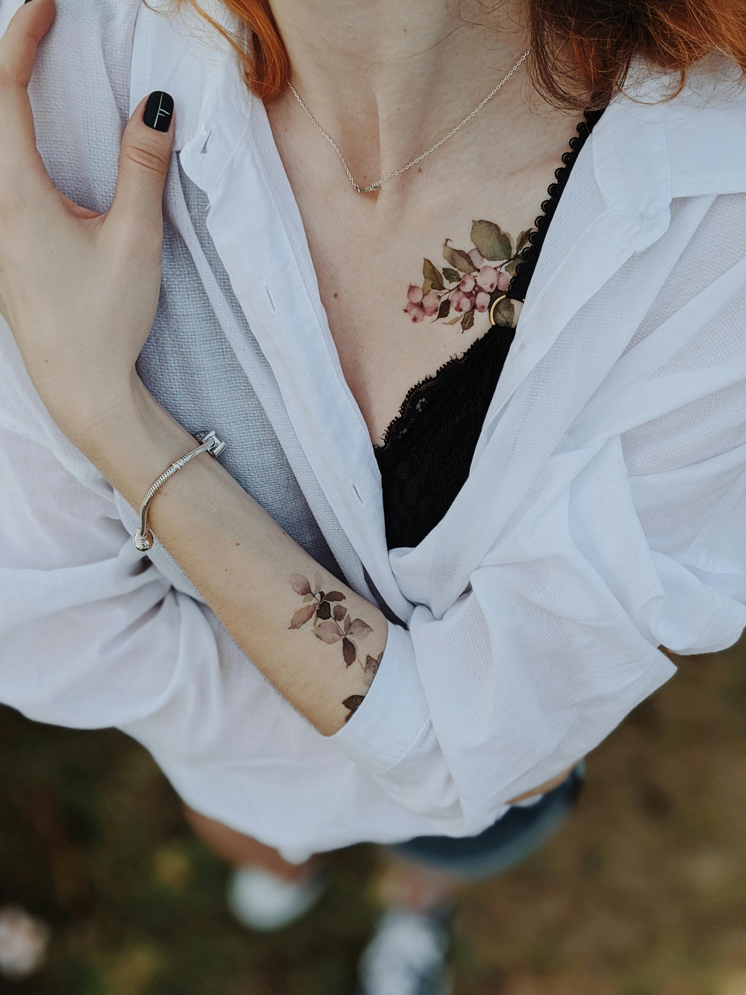 mulher de braço cruzado mostrando tatuagem floral delicada.